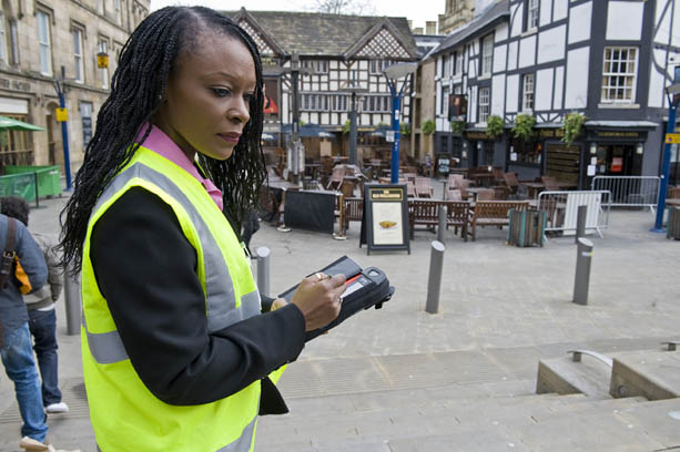 An image of a lady in a high vis jacket holding a clipboard in a public area