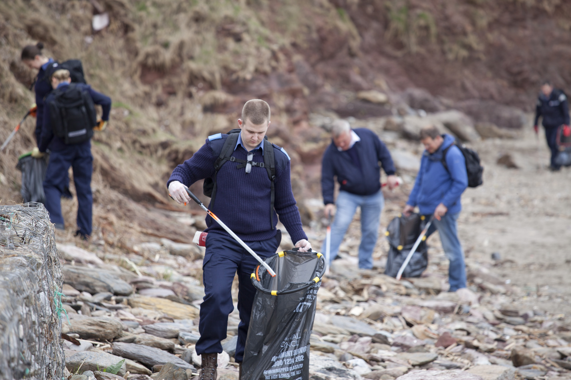 An image of a group of people collecting litter on a pebble beach