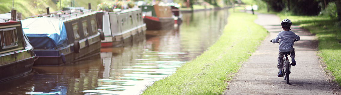 An image of a young child cycling down a canal path on a bicycle 