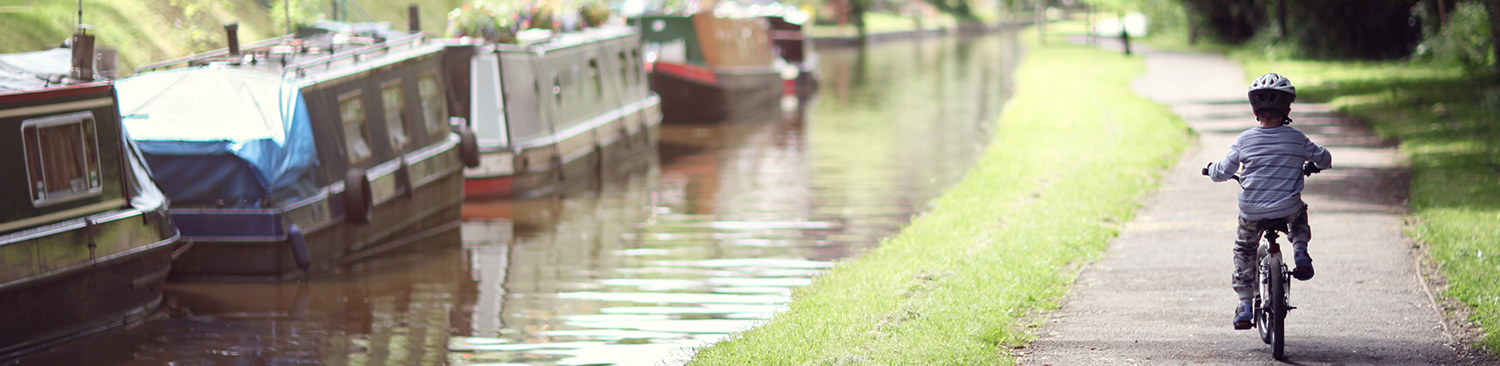 An image of a boy riding his bike along a canal