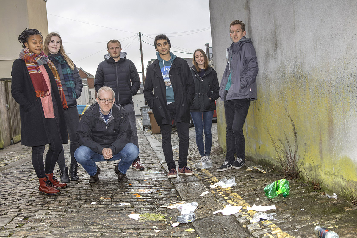 An image of university students standing outside surrounded by litter