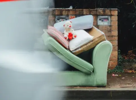 Fly-tipped sofa beside road with car going by